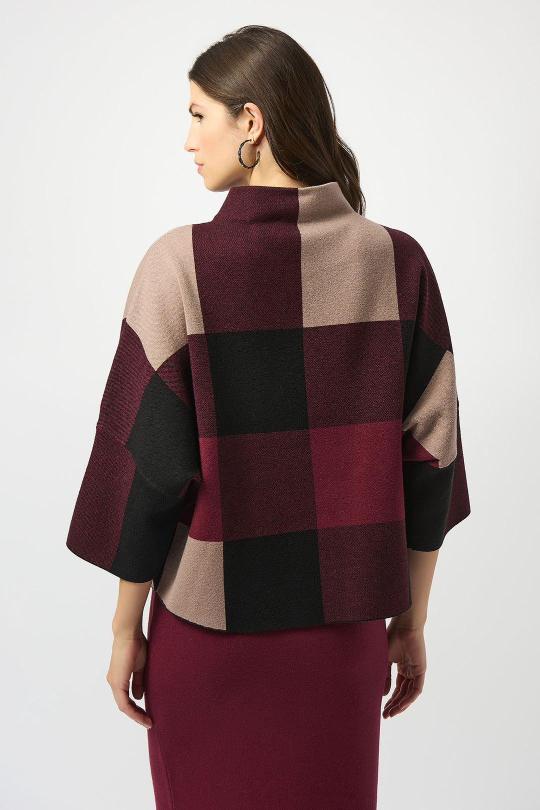 Woman wearing a checkered poncho with maroon, beige, and black pattern on a white background