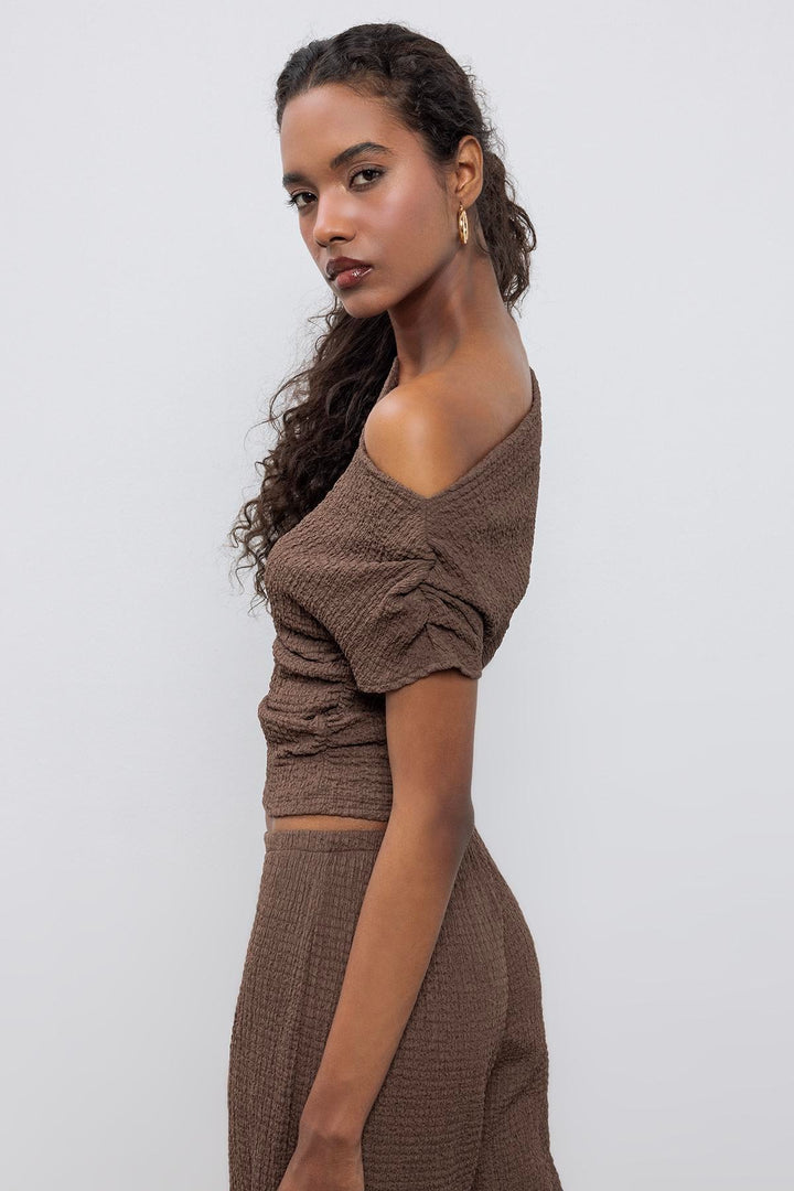 Side view of women's brown textured top with asymmetrical shoulder and elegant drape