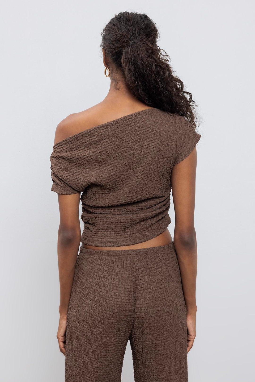 Back view of brown textured top featuring asymmetrical shoulder design and relaxed silhouette