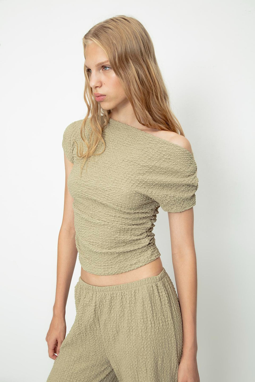 Side view of women's khaki textured top with asymmetrical shoulder and elegant drape