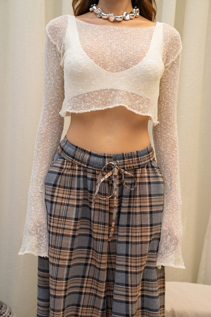 Person wearing a sheer long-sleeve top over a white crop top and plaid pants.