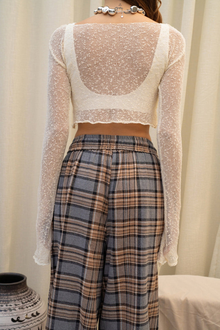 Person wearing a sheer long-sleeve top and plaid pants against a neutral background
