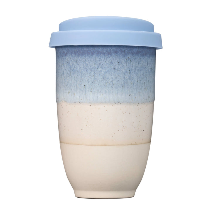 A reusable ceramic travel tumbler with a light blue lid, featuring a blue-to-cream gradient glaze with speckled detailing.