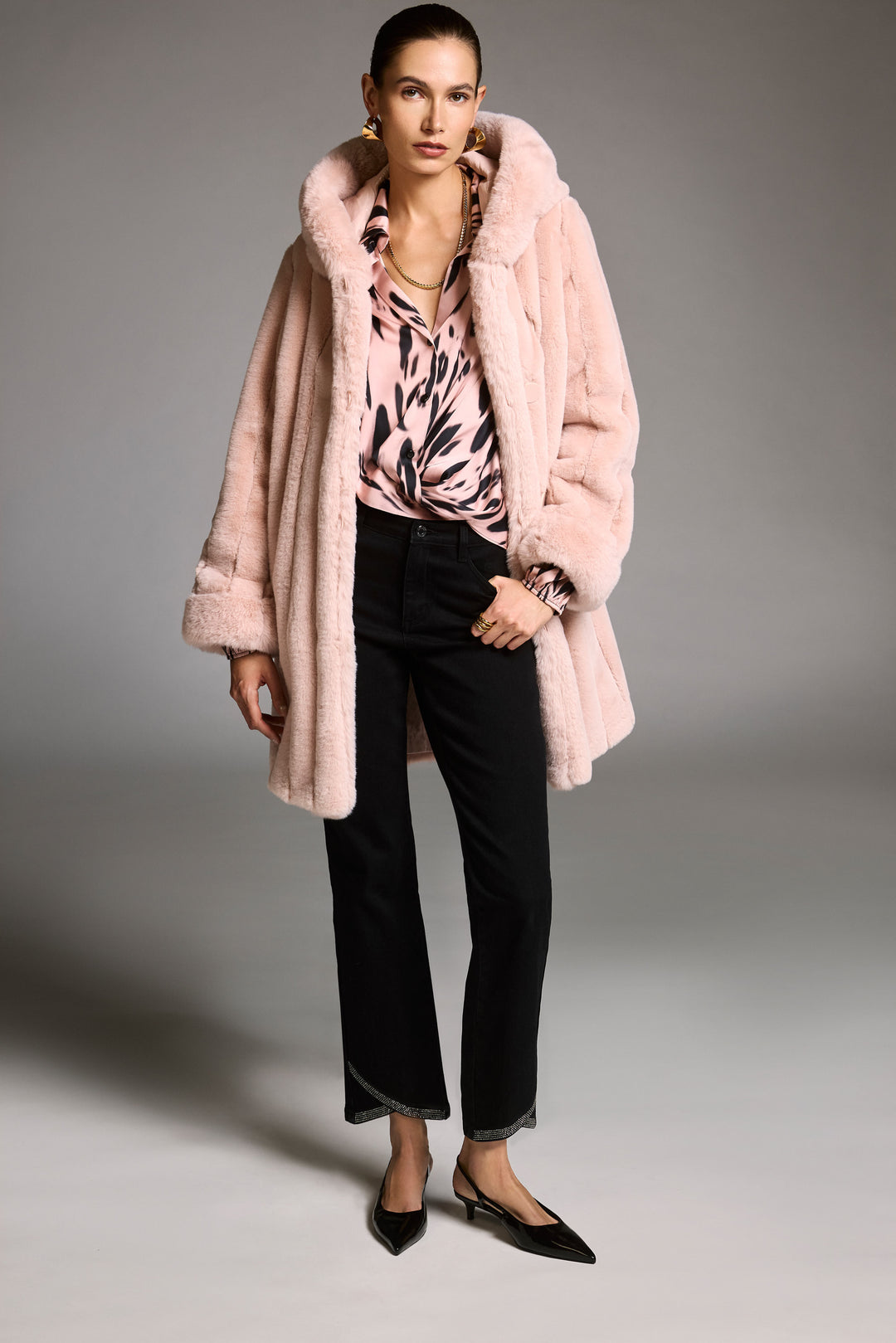 Woman wearing a pink fur coat, pink top, and black pants on a gray background