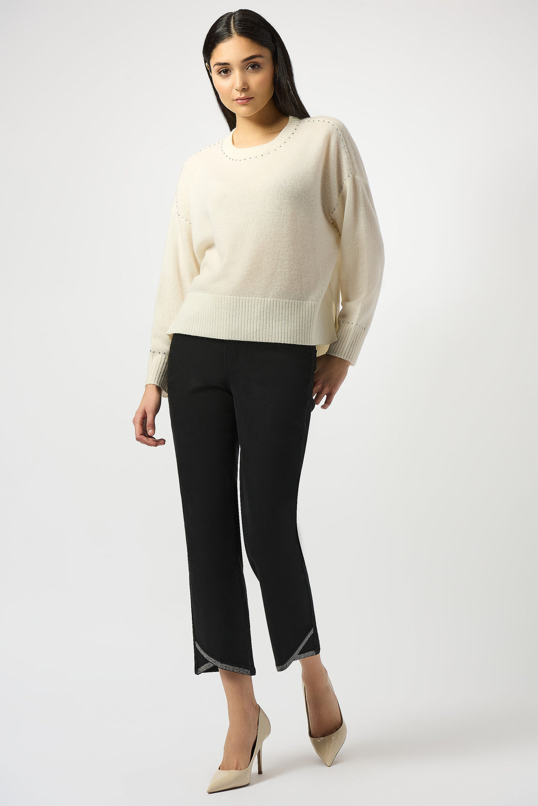Woman wearing a cream sweater and black pants on a white background