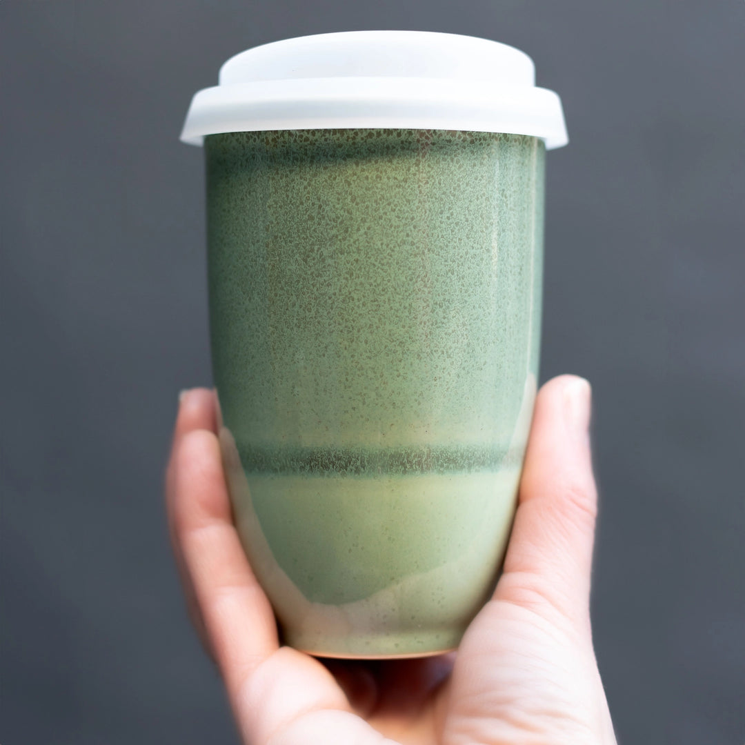 Hand holding a green ceramic cup with a white lid against a dark background
