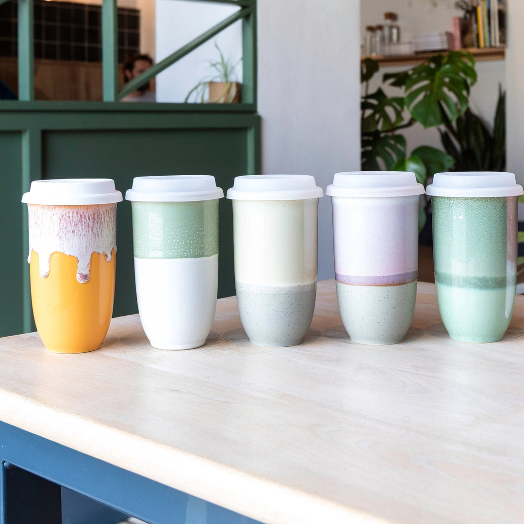 Set of colorful ceramic cups with lids on a wooden surface.