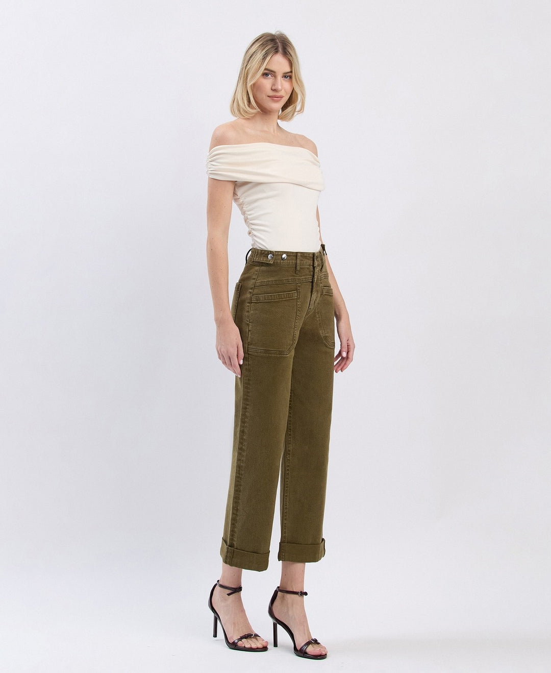 Woman wearing a white off-shoulder top and olive green pants on a white background