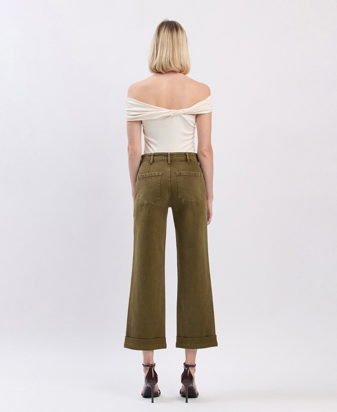 Woman wearing a white off-shoulder top and olive green wide-leg pants on a white background