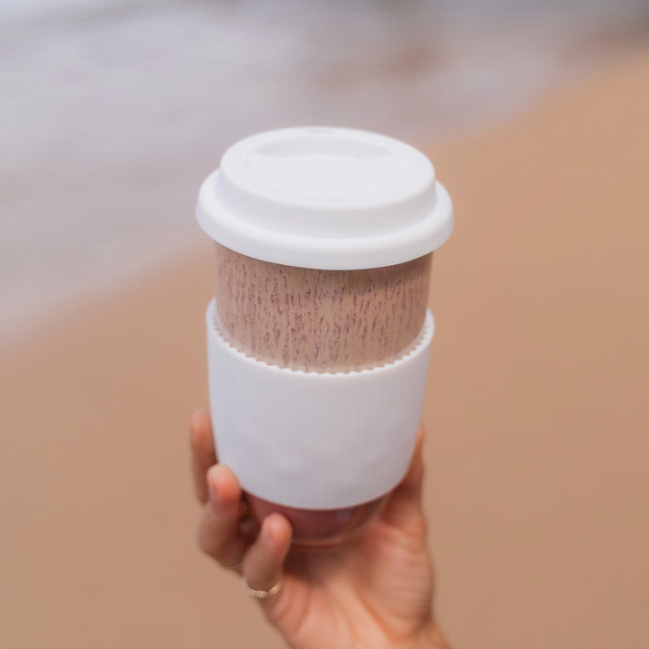 Hand holding a white coffee cup with a filter on a blurred background