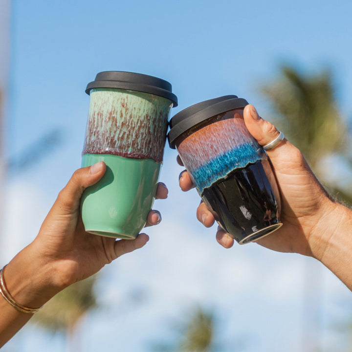Two hands holding colorful coffee cups against a blurred natural background