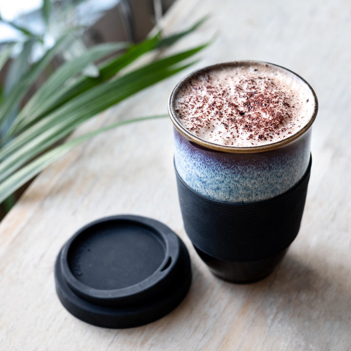 Black insulated coffee cup with a plant in the background