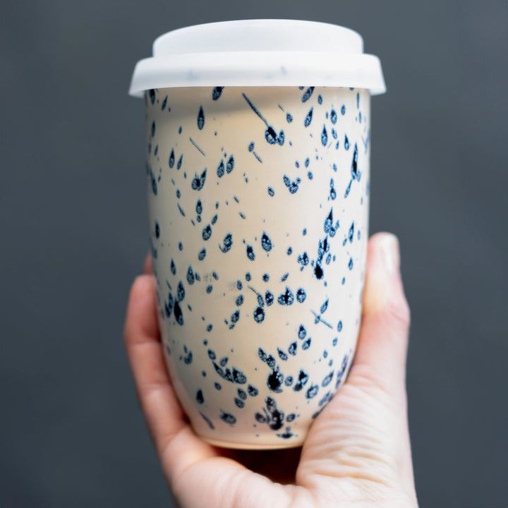Hand holding a paper cup with blue speckled design against a dark background