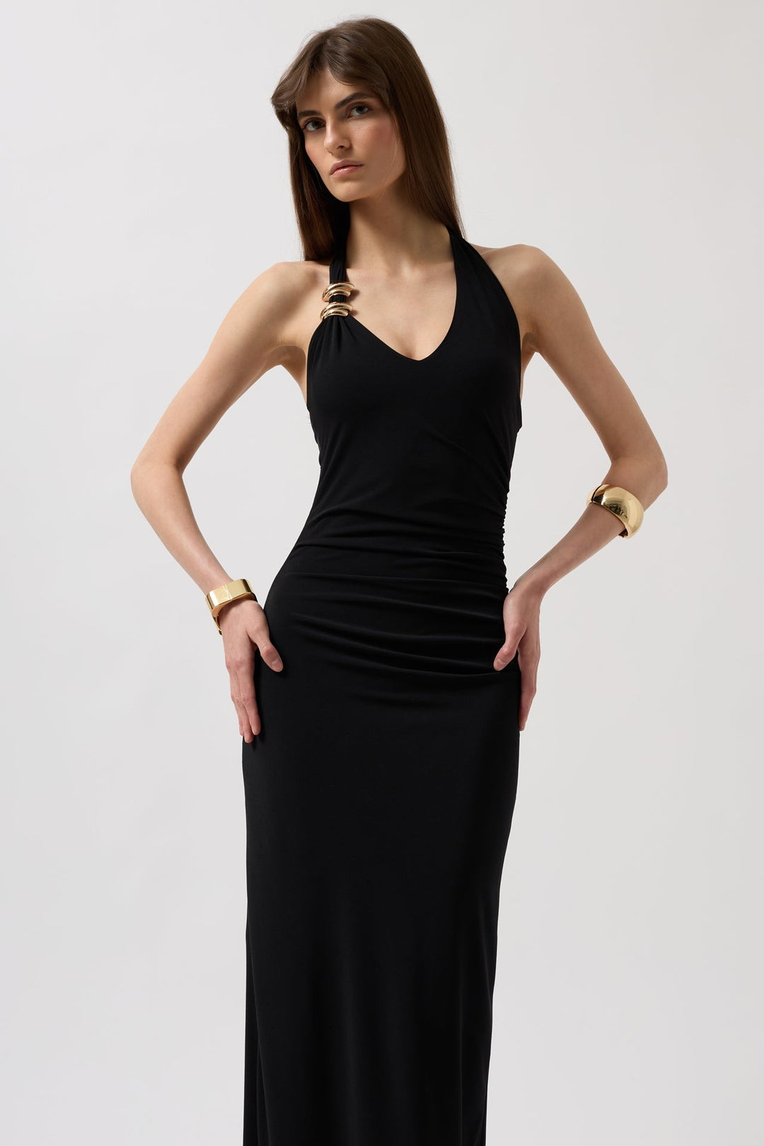 Woman wearing a black halter neck dress with gold accessories on a white background