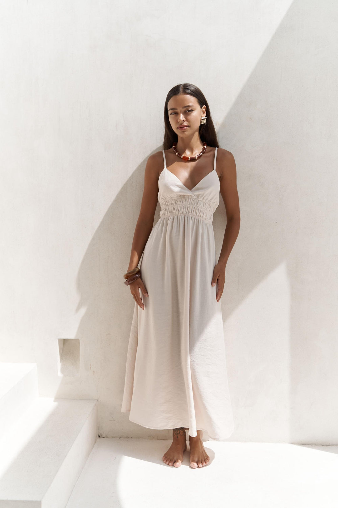 Woman wearing a white dress standing in a bright, minimalistic setting.