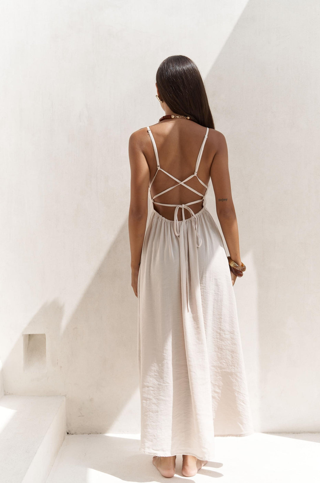 Woman wearing a white dress with a backless design in a bright, minimalistic setting.