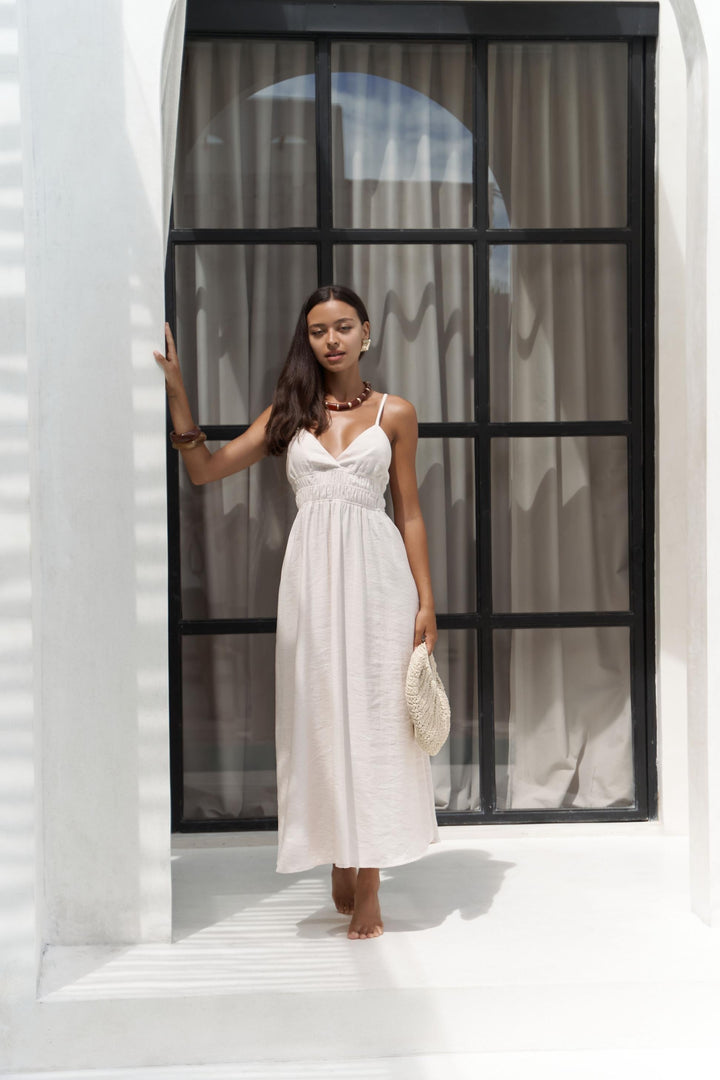 Woman in a white dress standing in front of a large window with a white wall and floor.