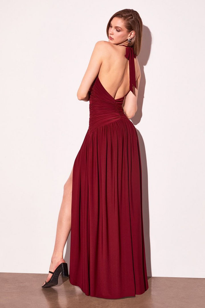 Woman wearing a burgundy evening gown with a slit on a white background