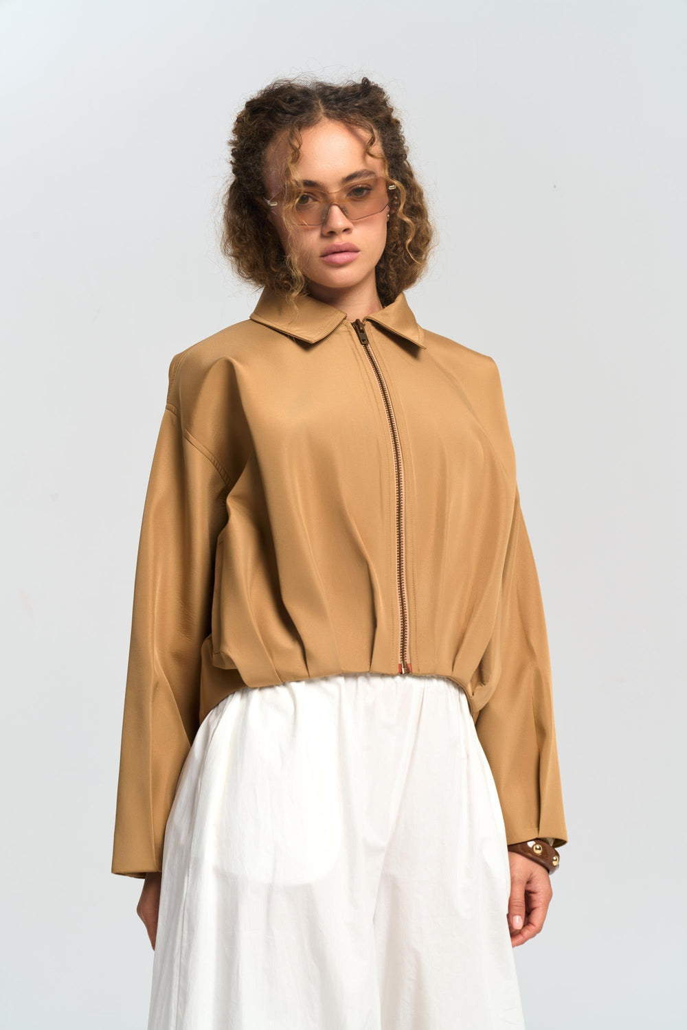 Woman wearing a tan jacket and white pants on a plain background