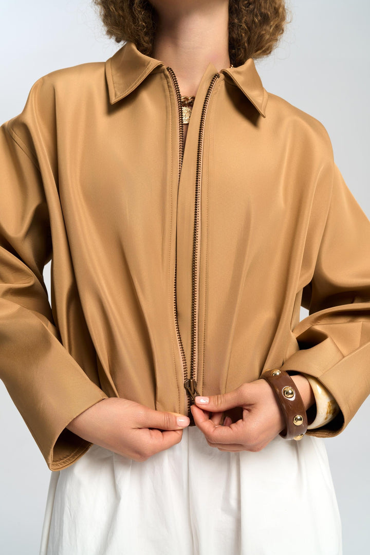 Person wearing a beige jacket with a zipper, holding it open against a light background