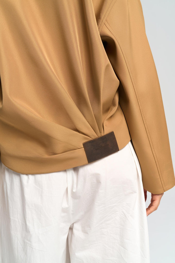 Close-up of a person wearing a beige jacket with a brown belt against a white background