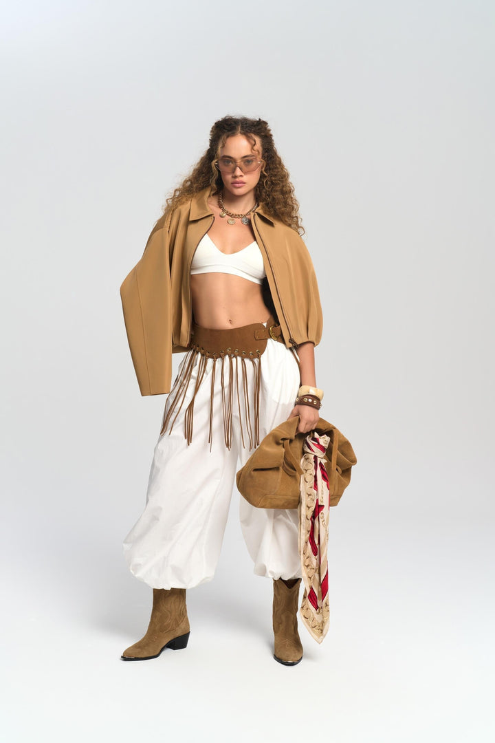 Person wearing a tan jacket, white top, and white skirt with brown boots on a white background