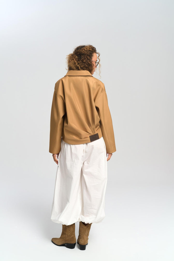 Person wearing a brown jacket and white pants on a plain background