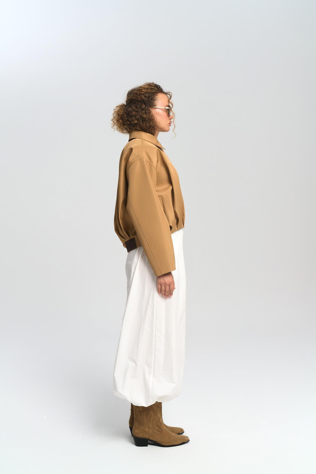 Person wearing a brown jacket, white pants, and brown shoes on a white background