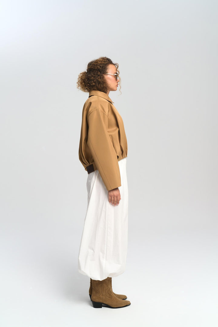 Person wearing a brown jacket, white pants, and brown shoes on a white background