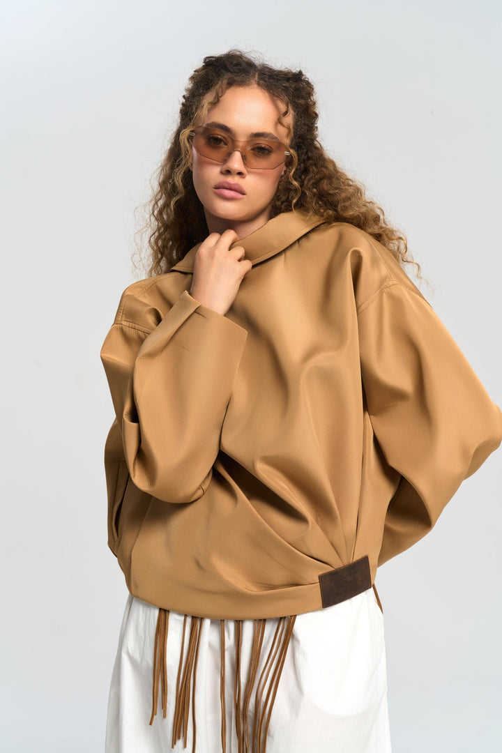 Woman wearing a tan poncho with fringe details on a white background