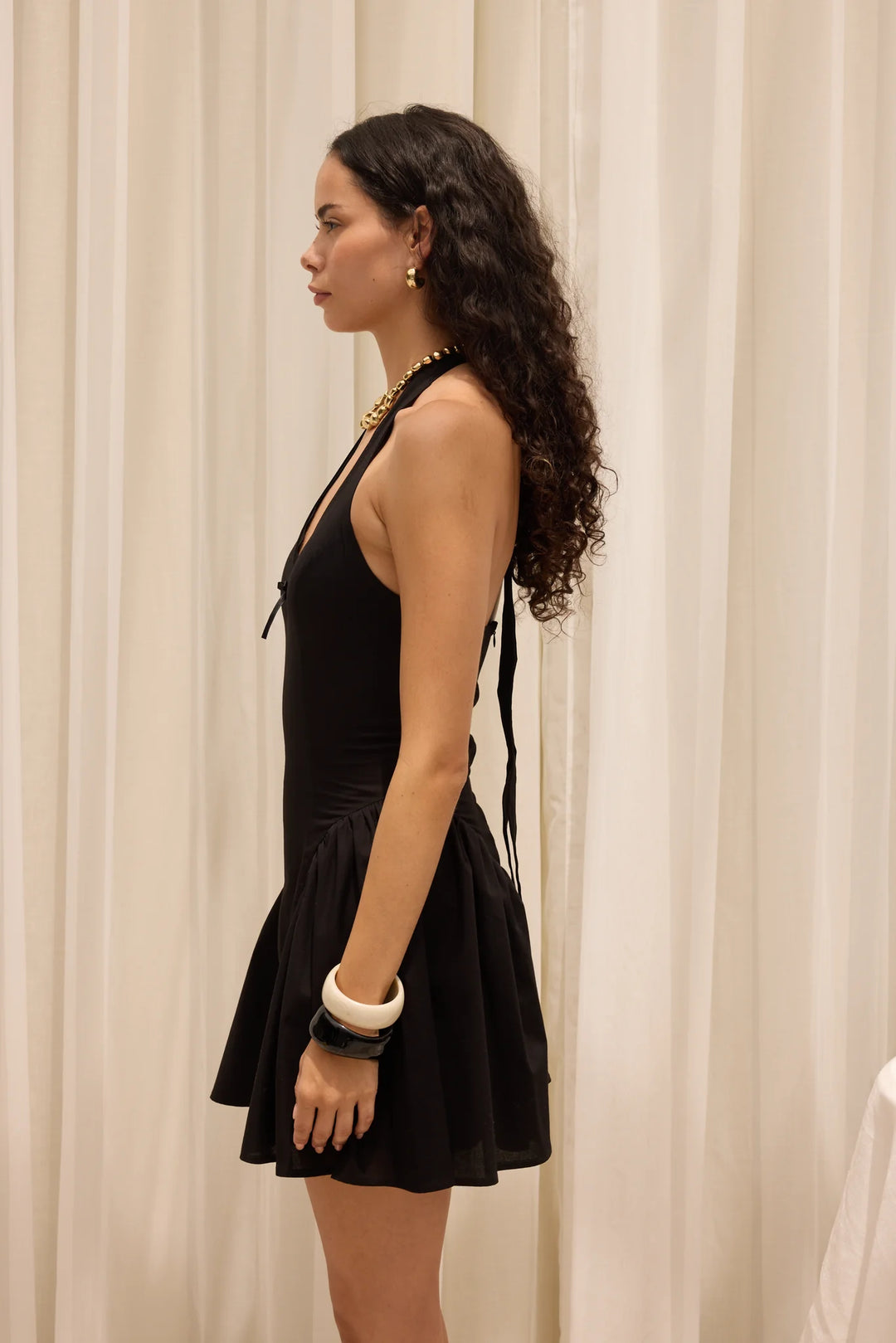 Woman wearing a black dress with a white curtain background