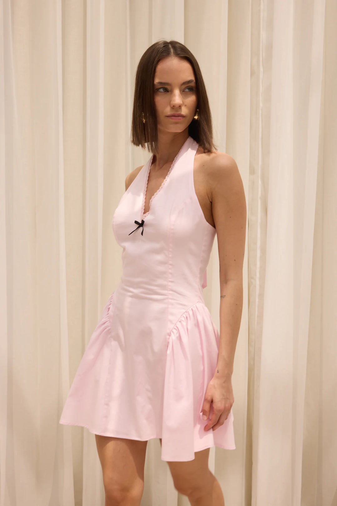 Woman wearing a light pink halter neck dress against a beige curtain background