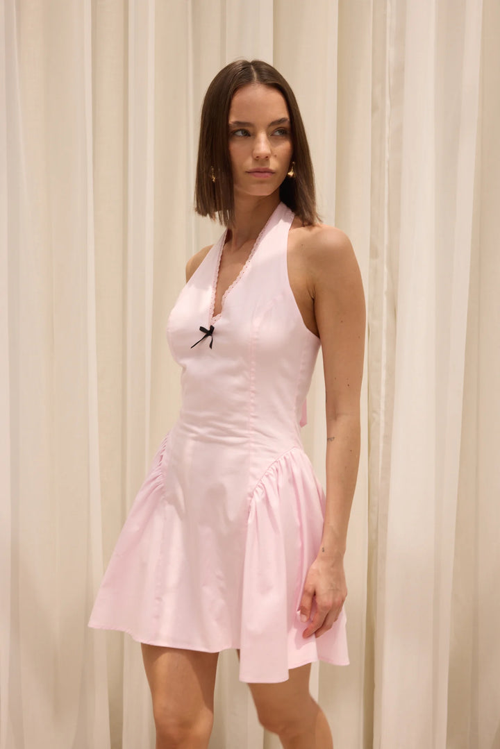 Woman wearing a light pink halter neck dress against a beige curtain background