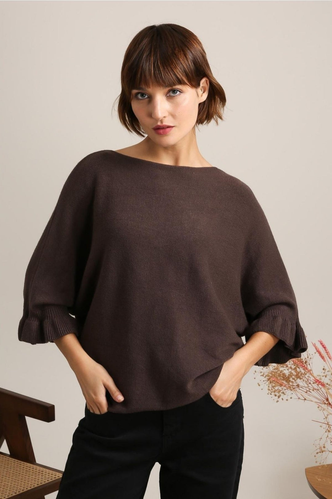 Woman wearing a brown sweater and black pants against a plain background