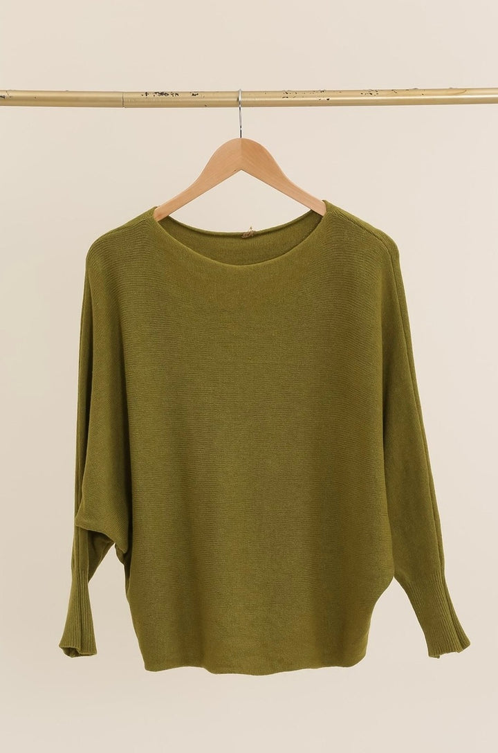 Green sweater on a wooden hanger against a beige background