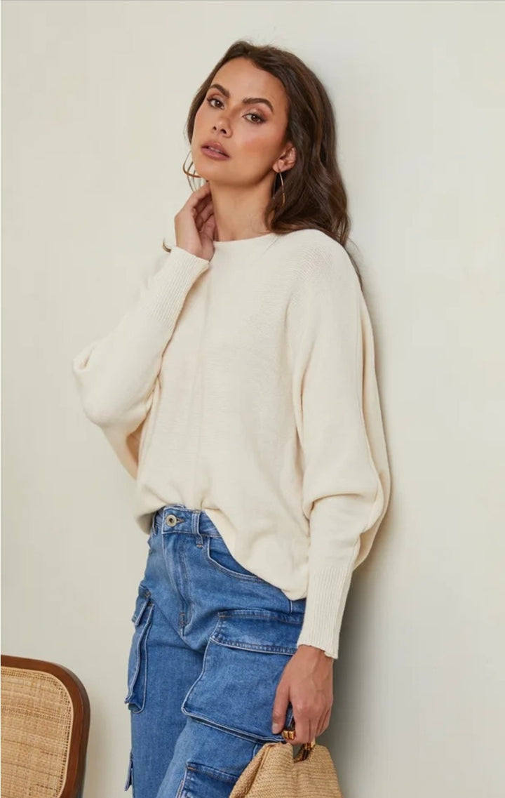 Woman wearing a cream sweater and blue jeans against a plain background