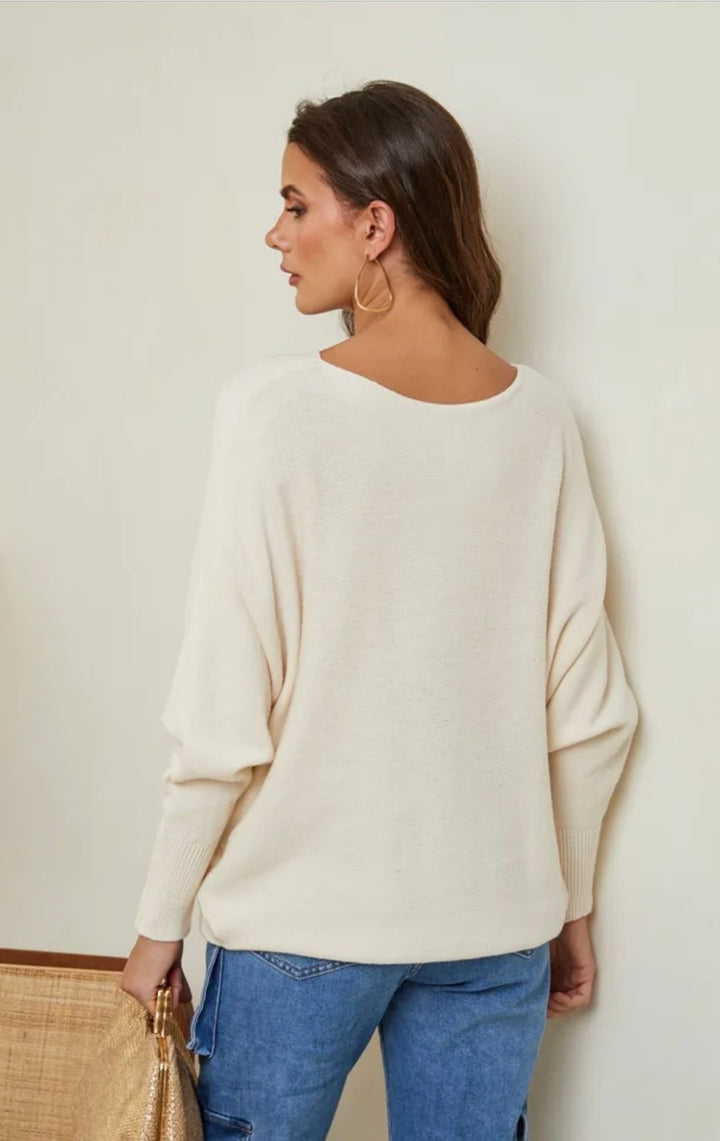 Woman wearing a beige sweater and blue jeans against a plain background