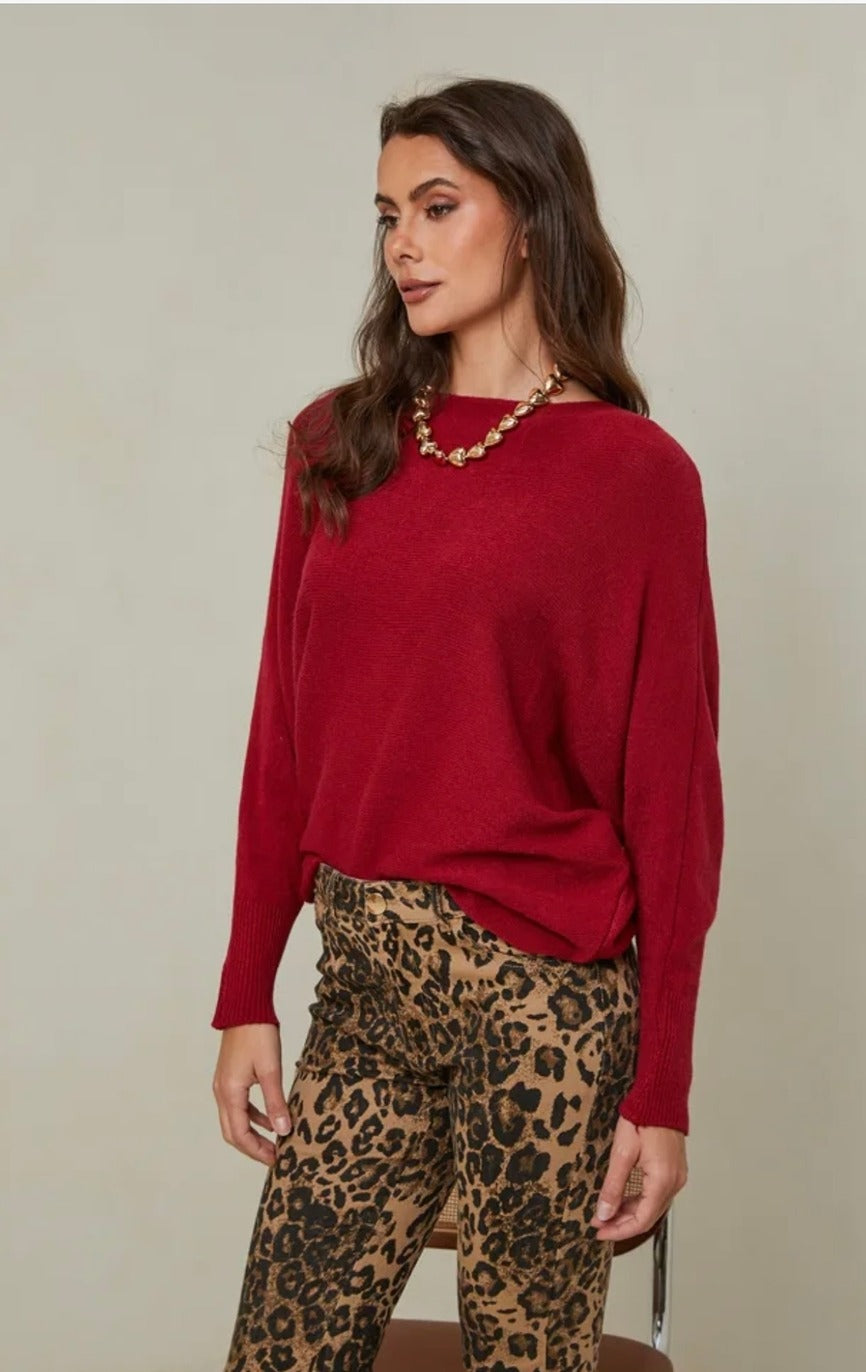 Woman wearing a red sweater and leopard print pants against a plain background
