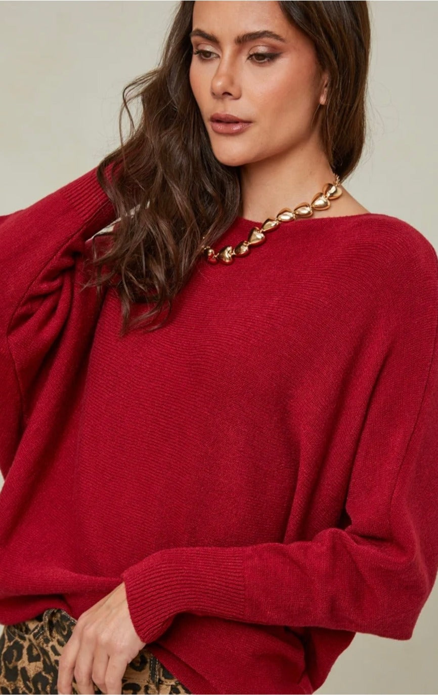 Woman wearing a red sweater with a gold necklace against a neutral background