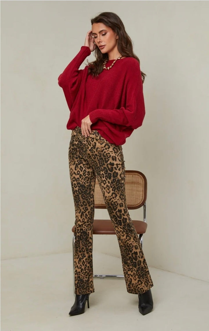Woman wearing a red sweater and leopard print pants sitting on a chair against a white background
