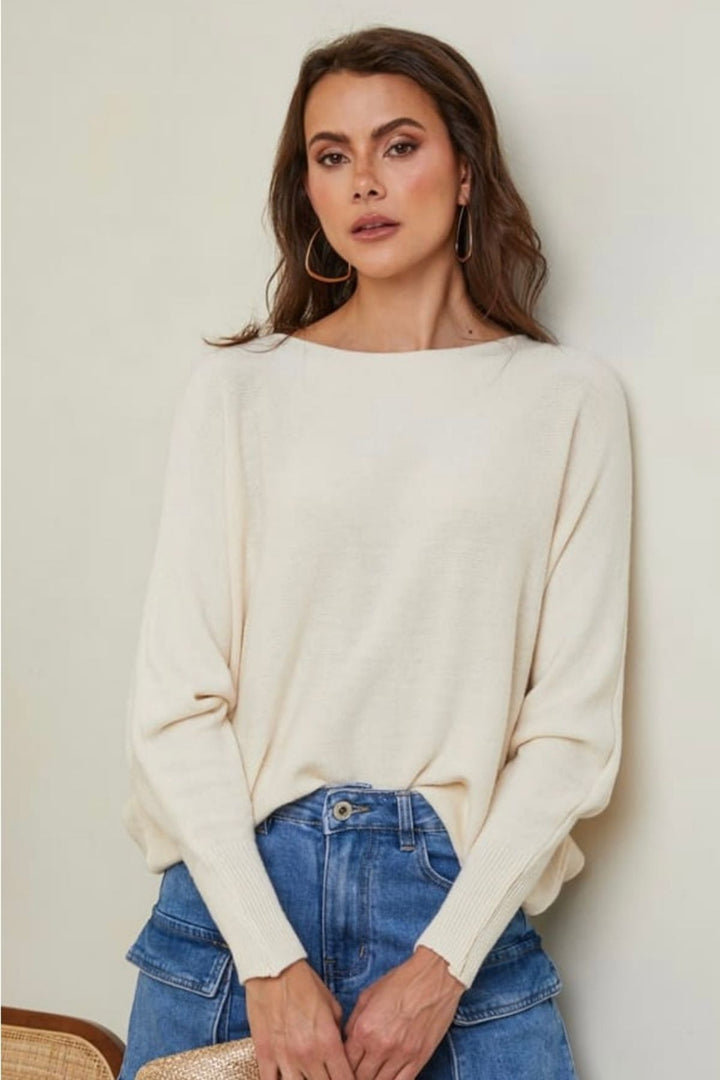 Woman wearing a cream sweater and blue jeans against a plain background