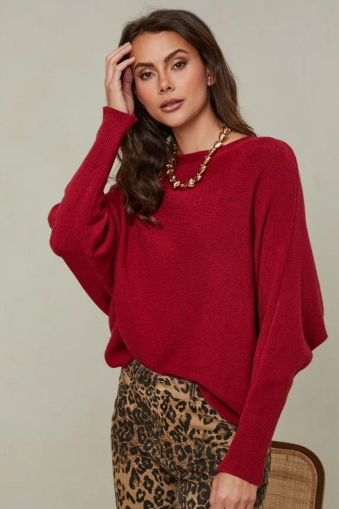 Woman wearing a red sweater and leopard print pants against a neutral background