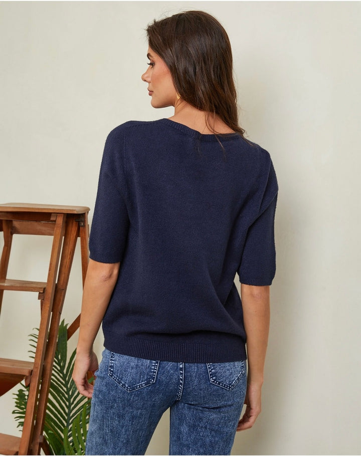 Woman wearing a navy sweater and blue jeans against a plain background