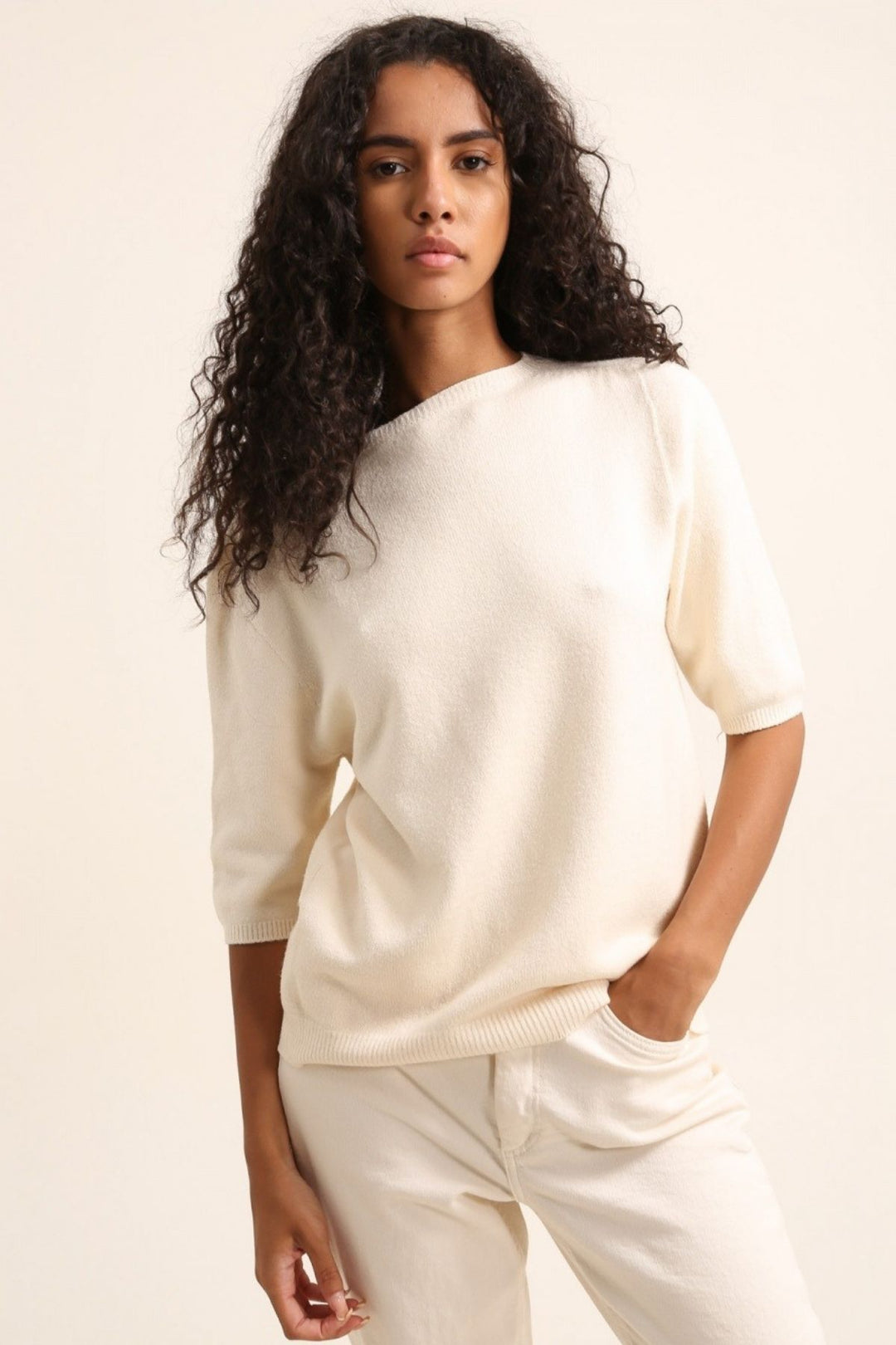Woman wearing a white sweater and pants against a plain background