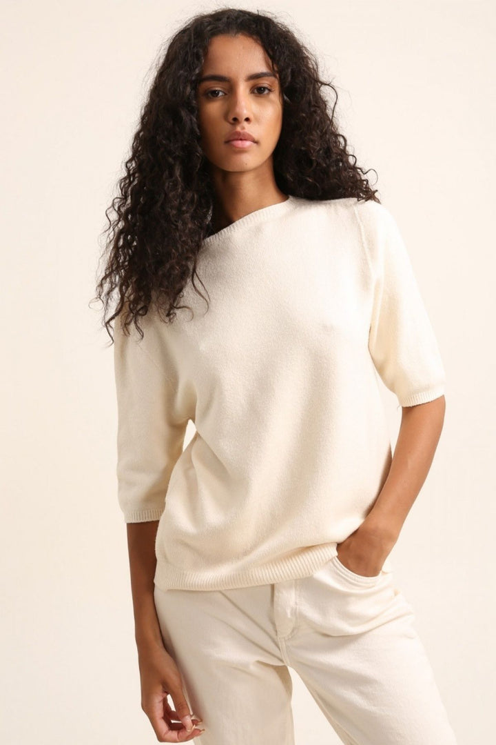 Woman wearing a white sweater and pants against a plain background