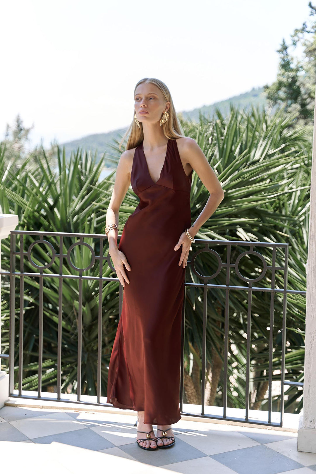 Woman in a burgundy dress standing on a balcony with greenery in the background