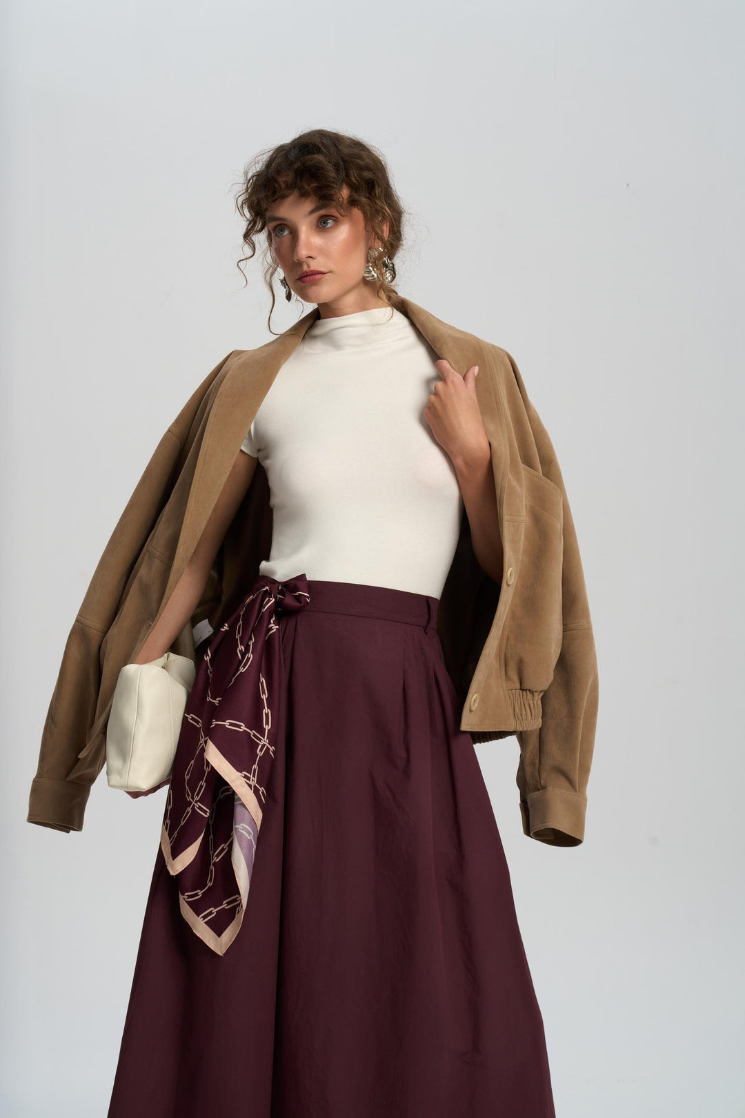 Woman wearing a brown jacket, white top, and burgundy skirt with a patterned scarf on a white background