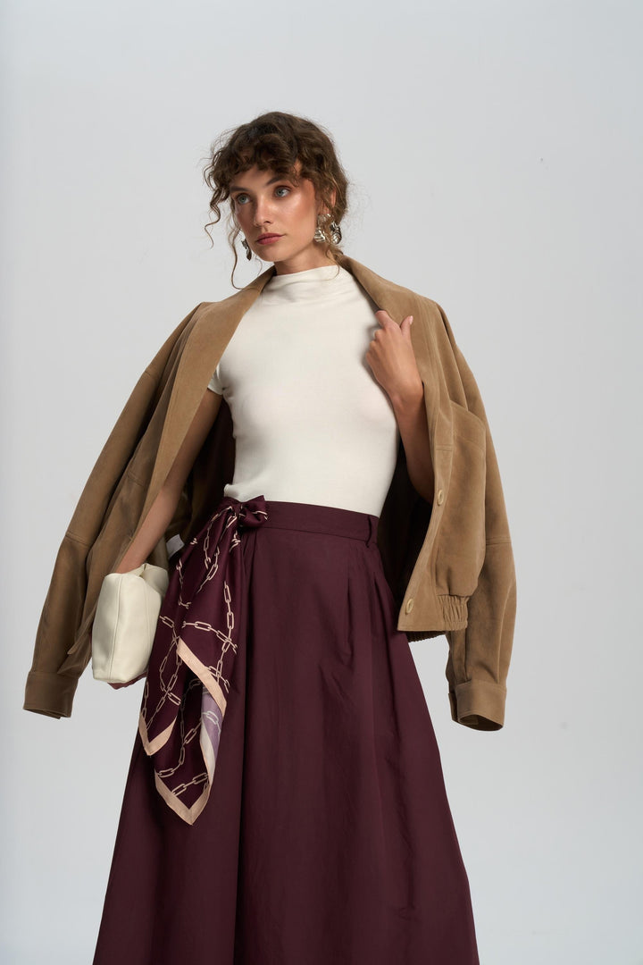 Woman wearing a brown jacket, white top, and burgundy skirt with a patterned scarf on a white background