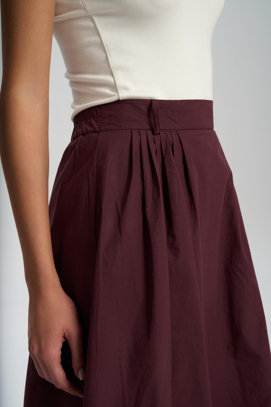 Maroon skirt worn with a beige top on a plain background