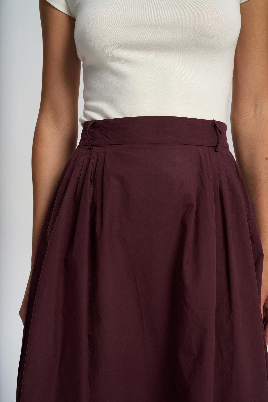 Person wearing a white top and maroon skirt on a plain background